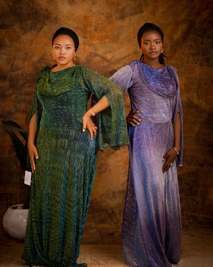 Two African women pose in elegant, colorful evening gowns against a rich backdrop.